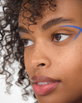 close up of a woman's face, with clear skin, curly hair, and bold blue eyeliner